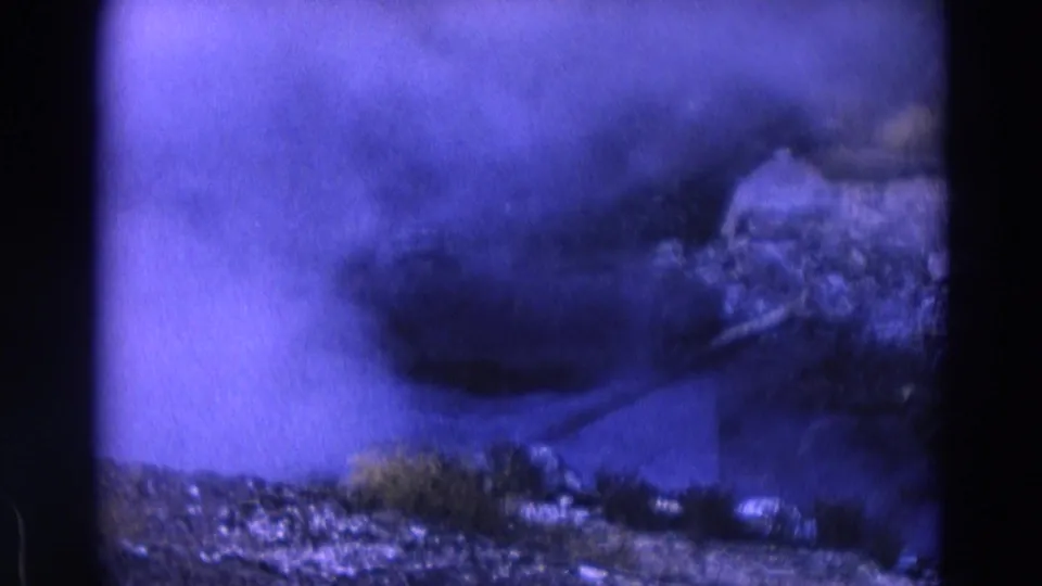 1967 Yellowstone 8mm frame with a thicker smoke or steam plume crossing rocky ground and low grasses.