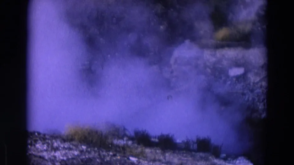 1967 Yellowstone 8mm frame showing a hazy smoke or steam cloud over rocky terrain, with grasses visible near the bottom edge.