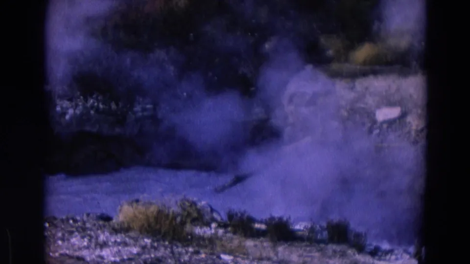 1967 Yellowstone 8mm frame with steam moving across rocks, scrub vegetation, and a small pipe or branch-like line.