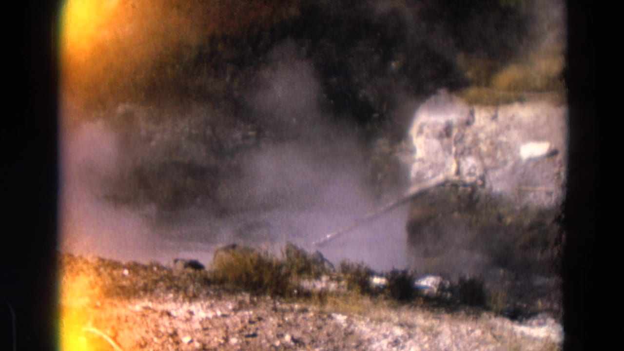 Geyser steam and spray rising across rocky ground with dark film edges.