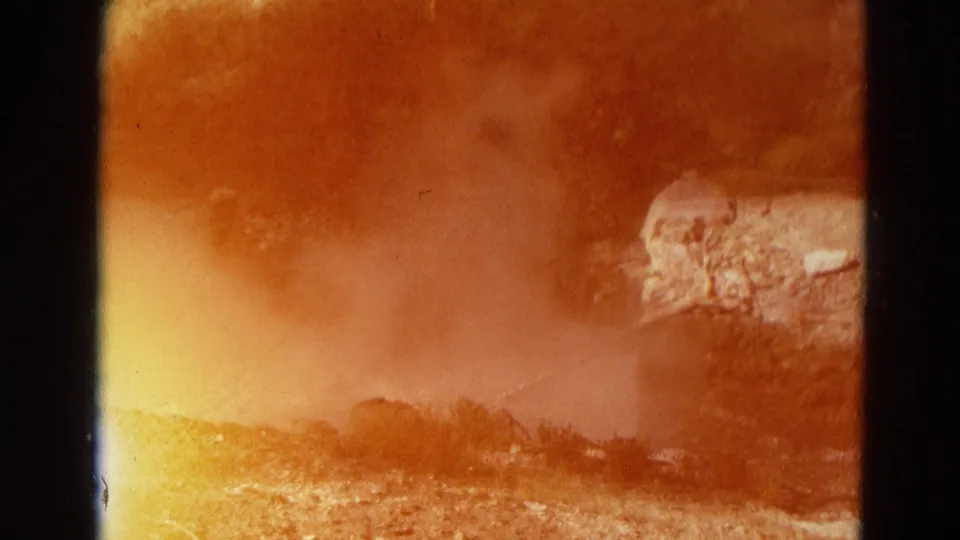 1967 Yellowstone 8mm frame where orange exposure flare partially obscures geyser steam, rocks and brush.