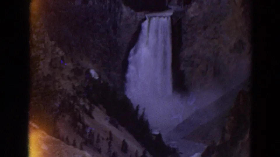 1967 Yellowstone 8mm frame showing a waterfall descending through a dark canyon with pine trees along the lower slope.