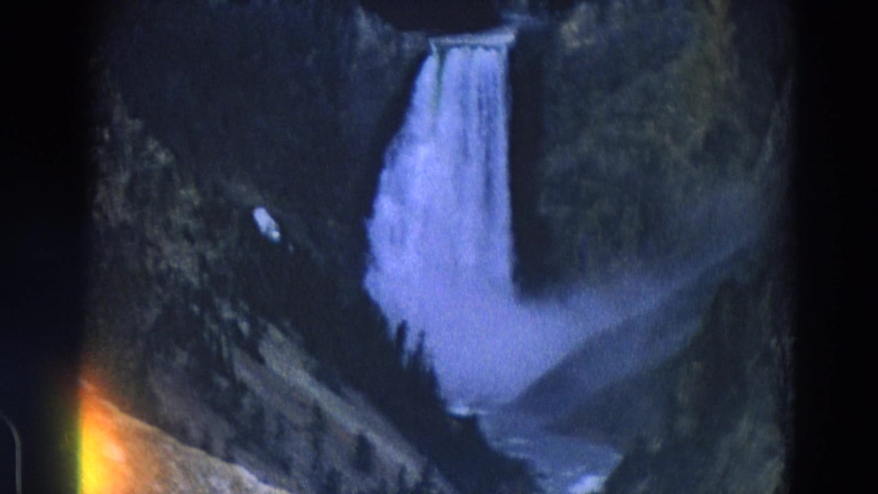 Waterfall framed by dark canyon slopes with a stream visible below.