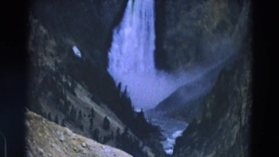 1967 Yellowstone 8mm frame with a tall waterfall, rocky foreground, dark trees, and a cool blue-purple film cast.