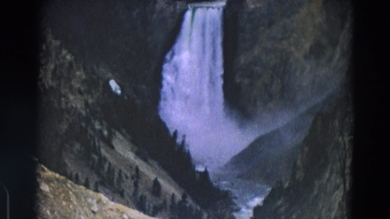 Wide view of a waterfall dropping into a misty canyon with trees and rocky slopes.