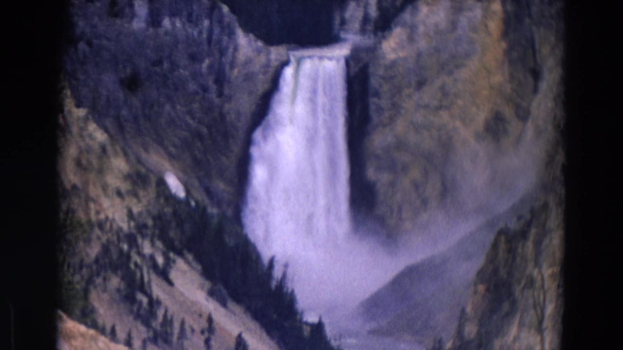1967 Yellowstone 8mm frame with a tall waterfall, heavy mist, forested canyon slopes, and rugged rock walls.
