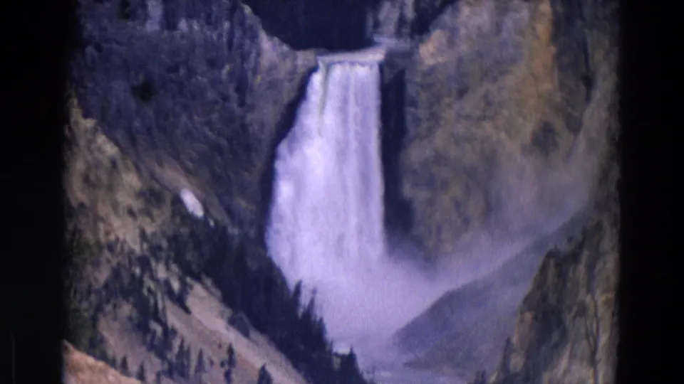 1967 Yellowstone 8mm frame with a tall waterfall, heavy mist, forested canyon slopes, and rugged rock walls.