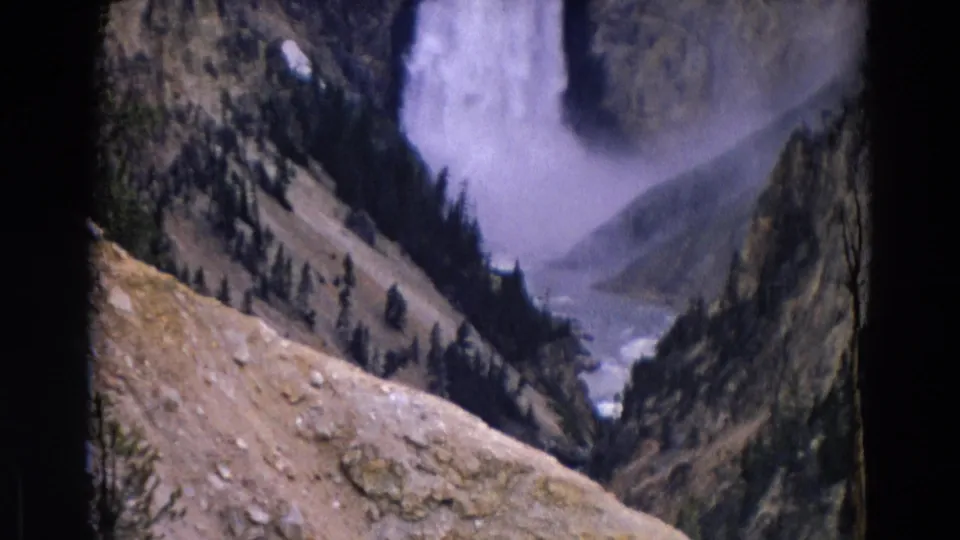 1967 Yellowstone 8mm frame showing the waterfall beyond a rocky foreground and descending canyon valley.