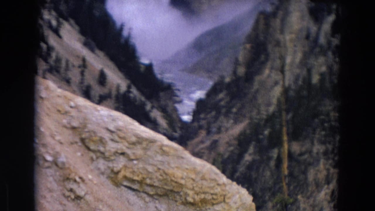 Canyon view with pale rock ledge, steep cliffs, evergreen trees, and distant water.
