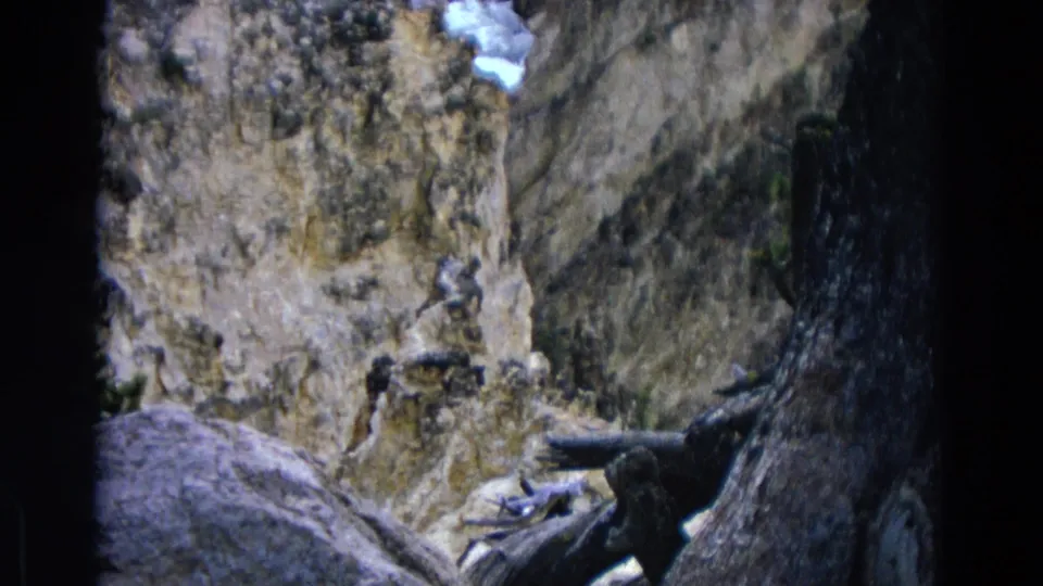 1967 Yellowstone 8mm frame looking across boulders and fallen timber toward a textured rocky cliff wall.