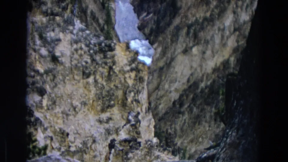 1967 Yellowstone frame showing a narrow rock crevice, steep cliff textures, dark tree edge, and a bright remnant of snow.
