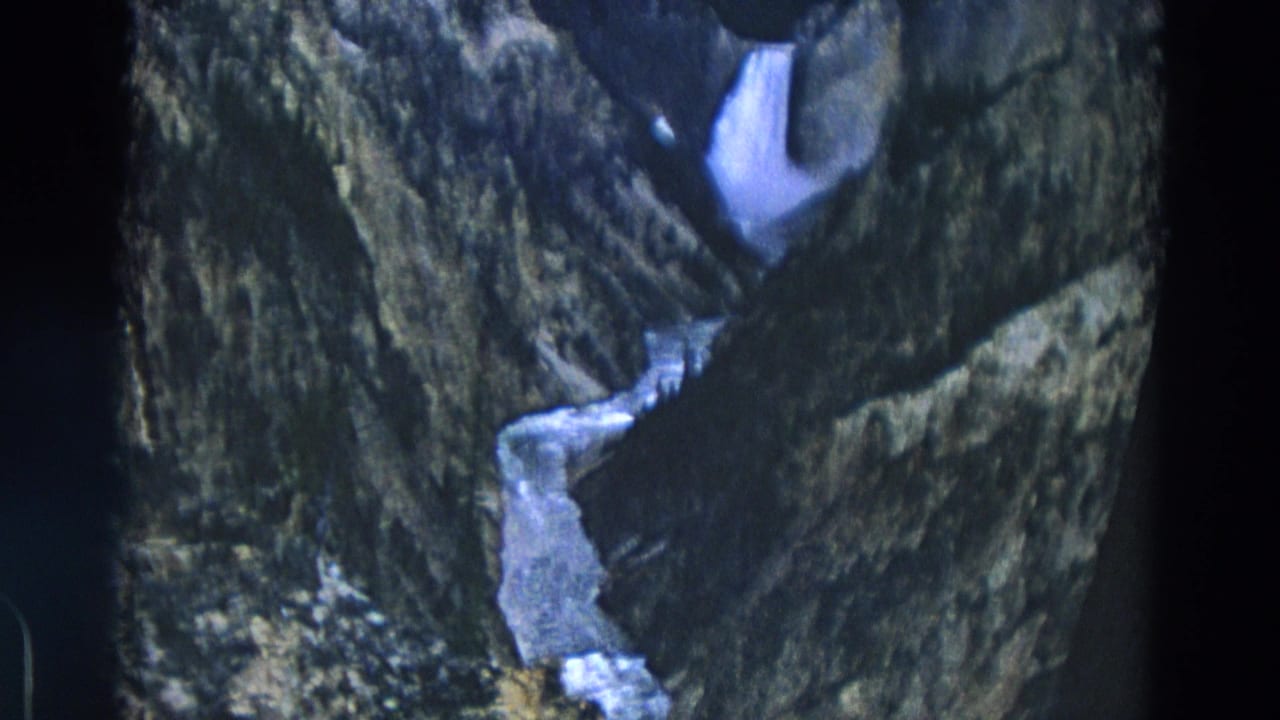 Narrow waterfall and stream cutting through a rocky canyon with dark film edges.