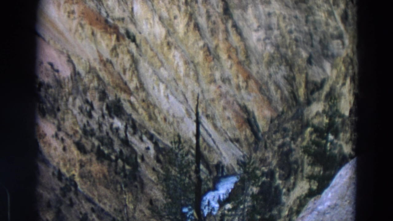 Steep canyon wall with evergreen trees and a small white waterfall near the lower edge.