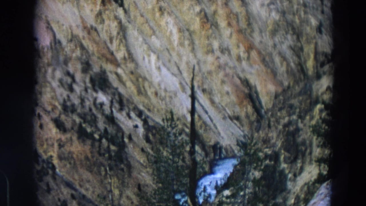 Yellowstone Park 8mm frame with layered canyon rock, sparse pines, and a bright cascade against the darker slope.