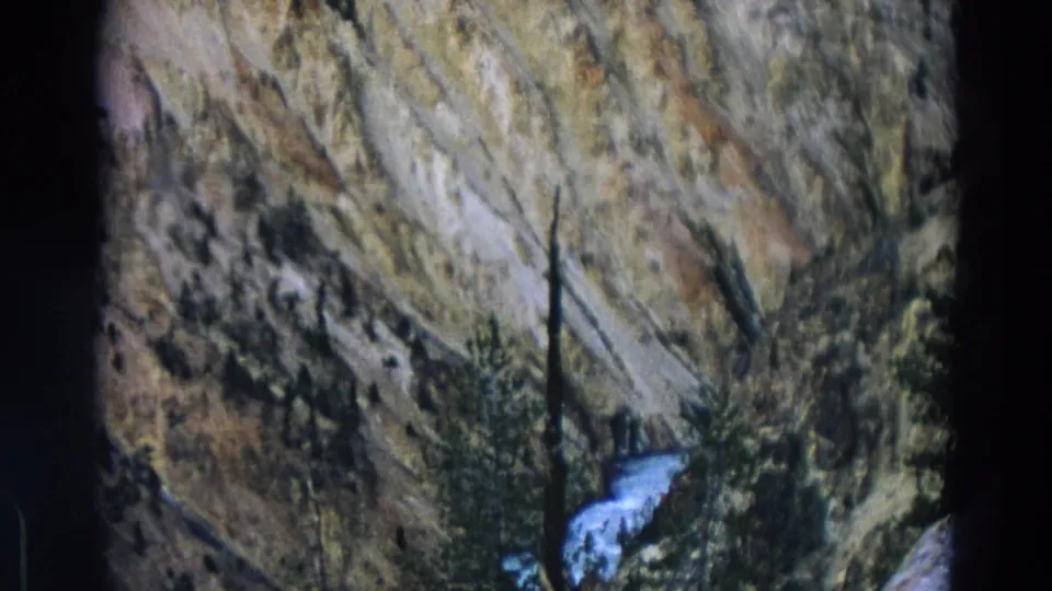 Yellowstone Park 8mm frame with layered canyon rock, sparse pines, and a bright cascade against the darker slope.