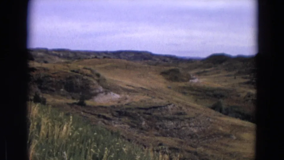 1967 Yellowstone frame showing a wide visitor-shot view of grassy hills and distant ridges beneath a soft overcast sky.
