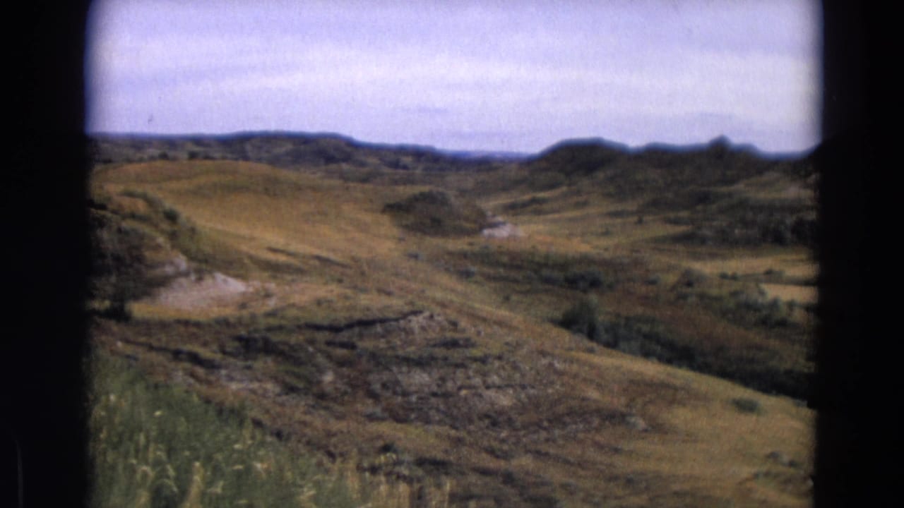 1967 Yellowstone view across muted grassland, rocky cuts, brush patches, and low hills in the distance.