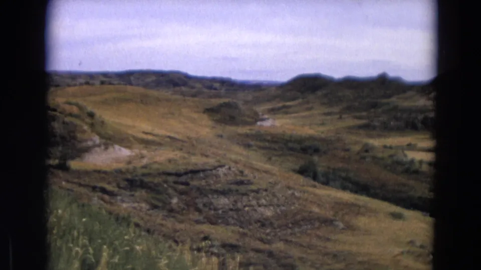 1967 Yellowstone view across muted grassland, rocky cuts, brush patches, and low hills in the distance.