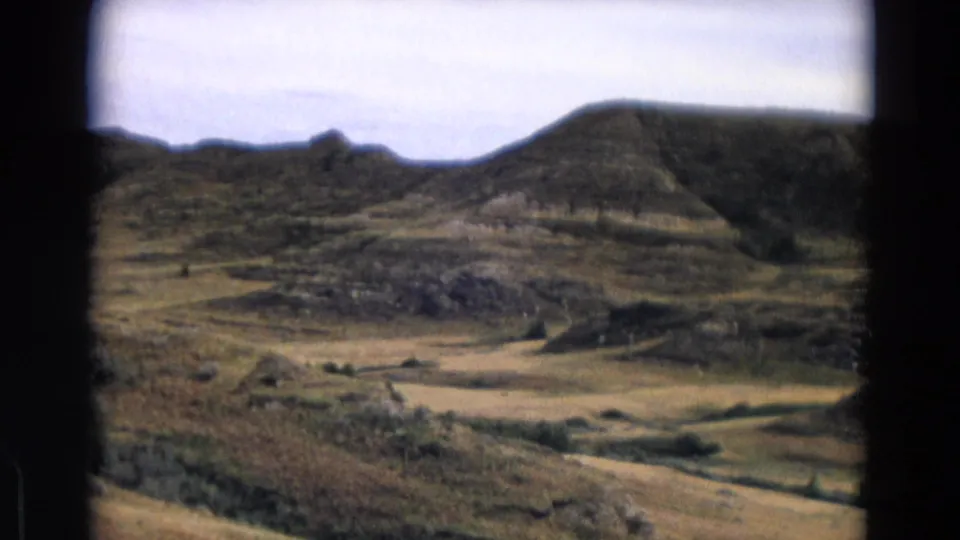 1967 Yellowstone-area 8mm frame showing layered hills, open dry valley, sparse vegetation, and a pale sky.