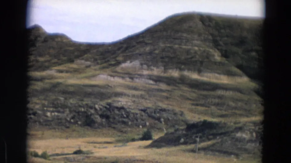 Yellowstone Park metadata frame showing a rounded hillside, exposed bands of earth, scattered brush, and dry valley terrain.