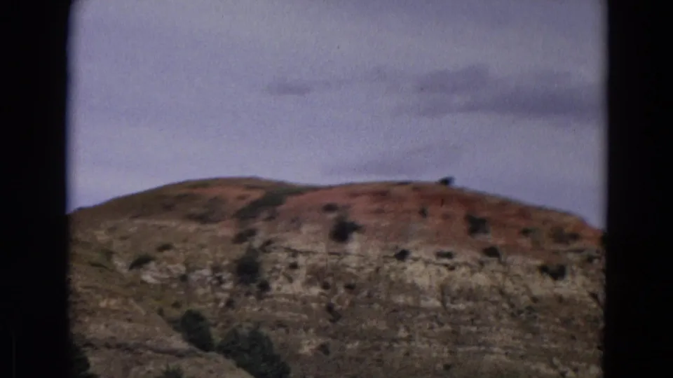 Final 1967 Yellowstone-area frame showing a rocky brown ridge, sparse shrubs, and muted sky in soft 8mm color.