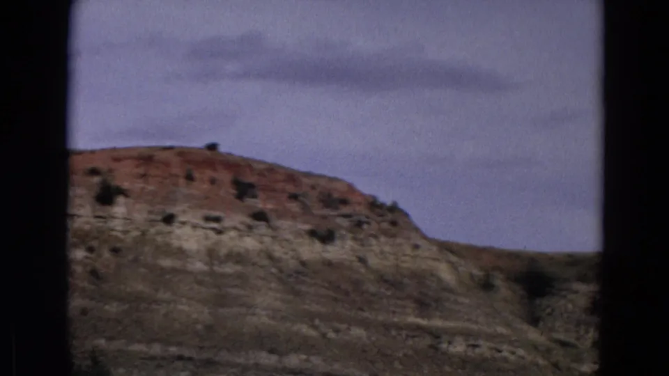1967 Yellowstone frame with a rocky ridge, reddish upper layers, scattered shrubs, and visible 8mm gate edges.