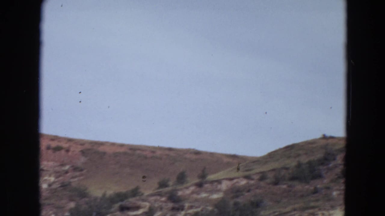 Brown hills under a pale sky seen through dark vertical film borders.