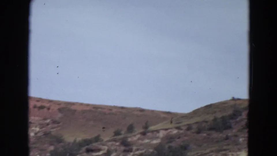 1967 Yellowstone-area 8mm frame showing rolling winter hills under a pale sky, partly obscured by dark window-like borders.