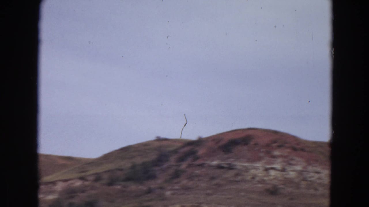 Rugged brown hillside beneath a pale sky with dark frame borders.