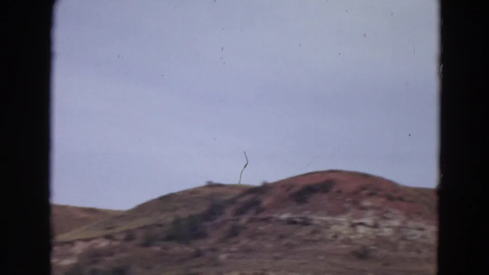 1967 Yellowstone-area view of a rugged hillside and muted sky, captured on grainy 8mm film from a partially blocked vantage point.