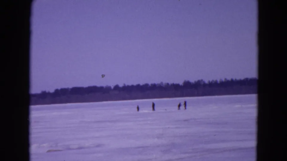 1967 Yellowstone-area frozen lake scene with distant ice fishermen standing on the snow-covered surface near a dark tree line.