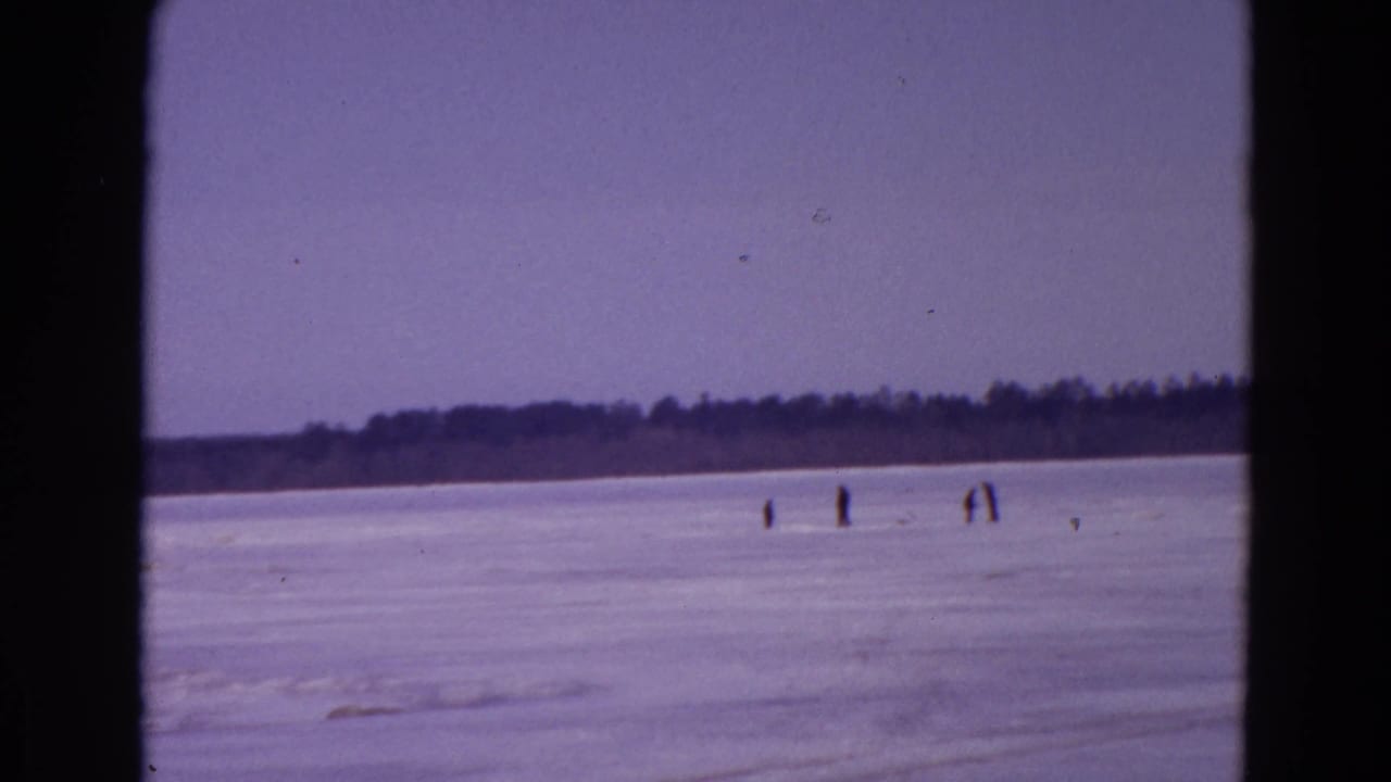 Wide frozen lake scene with several tiny figures spaced across the ice near the horizon.