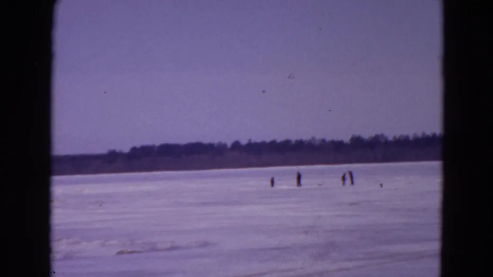 Wide 1967 Yellowstone winter view with small figures on the ice, a distant wooded shoreline, and visible film borders.