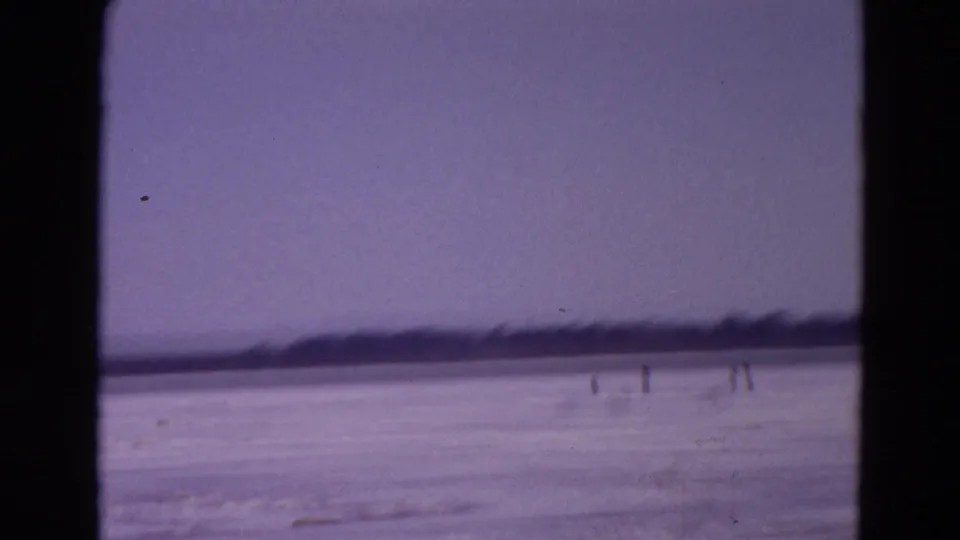 Soft 8mm Yellowstone winter frame with faint human figures on the frozen lake and a dark shoreline in the distance.