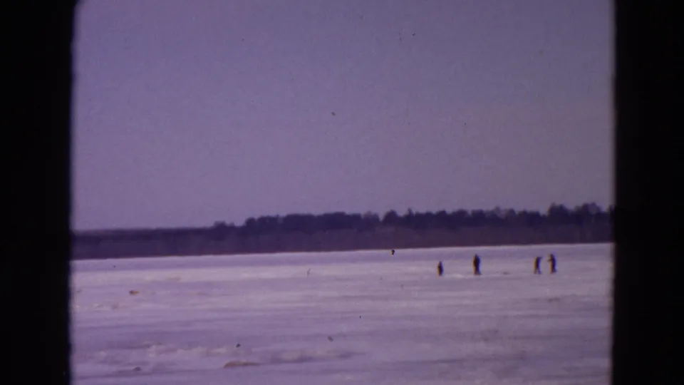 1967 Yellowstone winter home-movie frame showing small groups of people on a frozen lake near a distant shoreline.