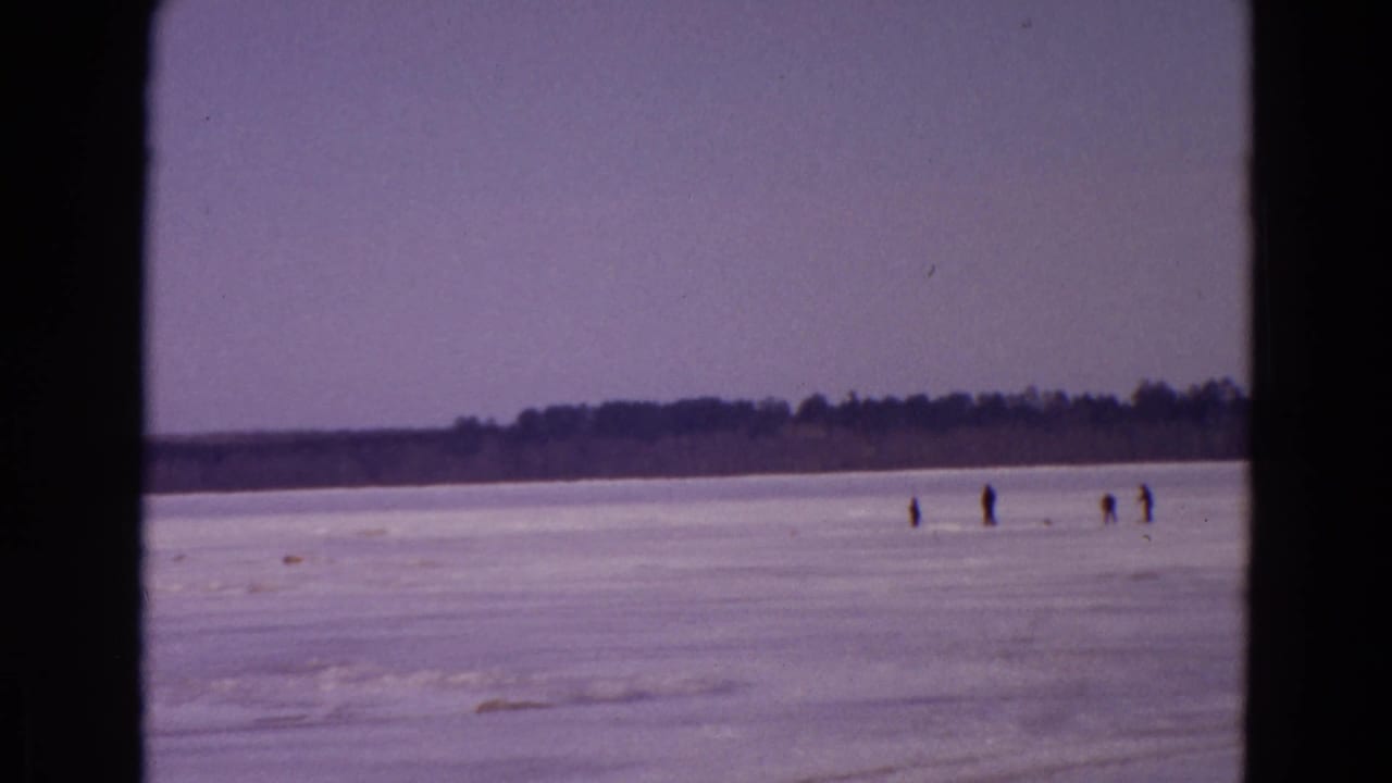 Frozen lake with small distant figures walking on the ice and a dark tree line beyond.