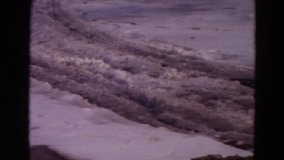1967 Wyoming home-movie frame of rough ice and snow along a frozen lake, framed by dark film borders.