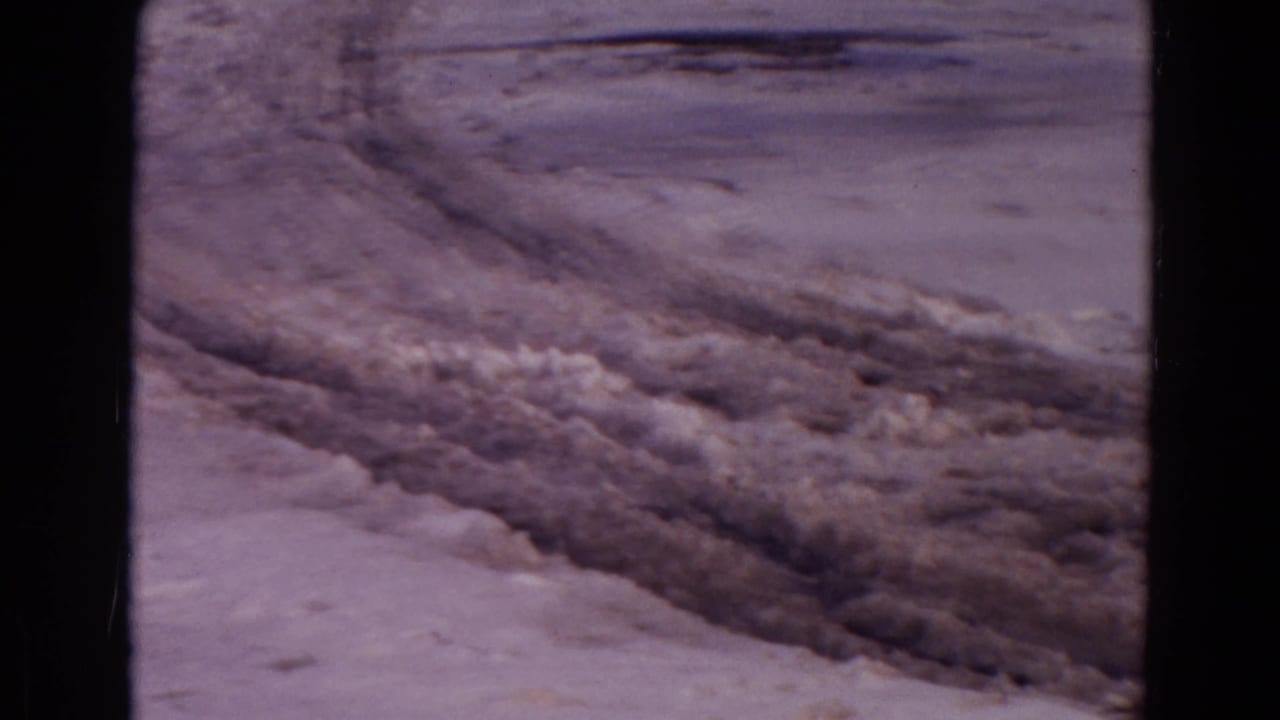 Snow-dusted dirt road with deep tire ruts crossing a barren surface.