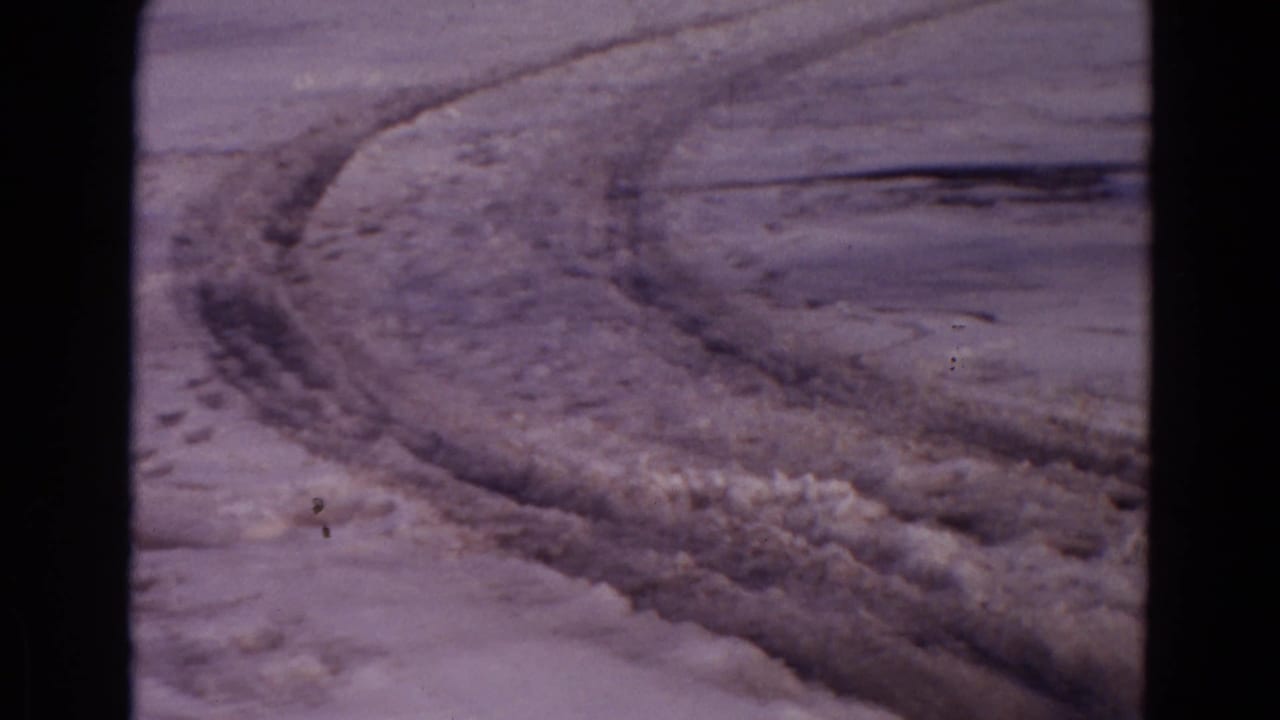 Curving tire tracks and churned snow on a rough dirt road.