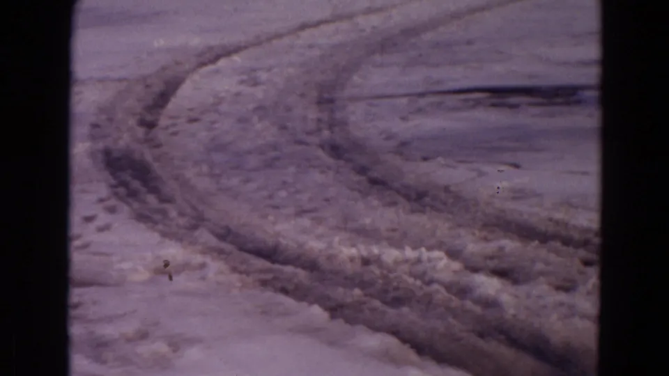 1967 Yellowstone home-movie frame with curved tire tracks through snow and muddy ground.