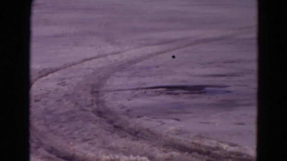 1967 8mm Yellowstone footage shows curved tire tracks cutting through a wide frozen snowfield beneath a muted sky.