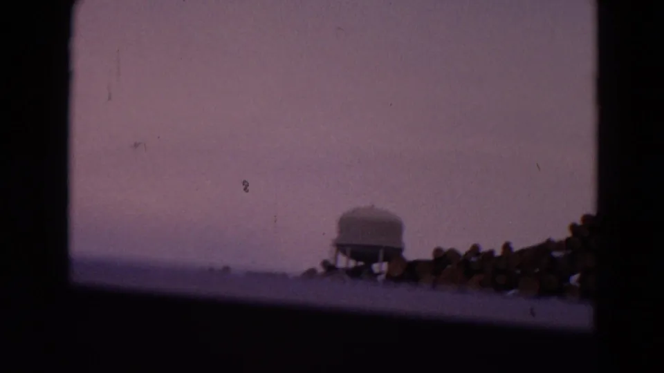 The 1967 8mm frame shows a small tank or water tower near timber piles, viewed through a window in Wyoming travel footage.