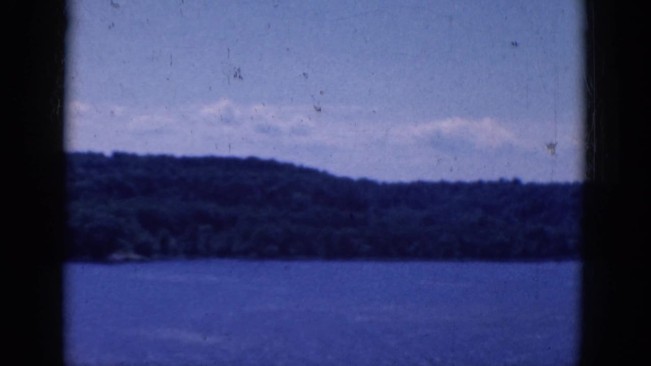 Blue-toned water and a wooded hillside seen through dark vertical window framing.