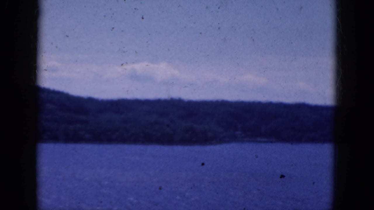 Distant forested shore across blue water with dark framing at both sides.