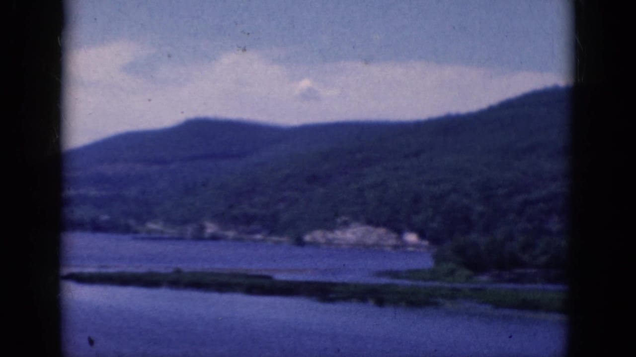 Lake shoreline and wooded hills divided by a dark vertical film edge.