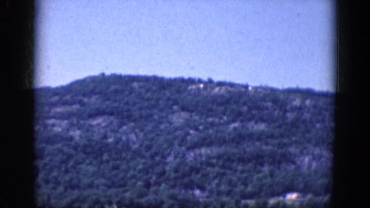Forested mountain ridge under blue sky within dark film borders.