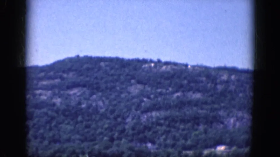 1968 8mm frame from a landscape pan, showing a wooded ridge and open blue sky with no people visible.