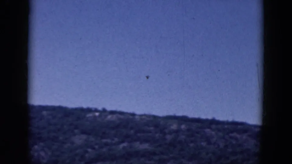 1968 home-movie frame showing mostly blue sky above a low, tree-covered ridge during the end of the pan.