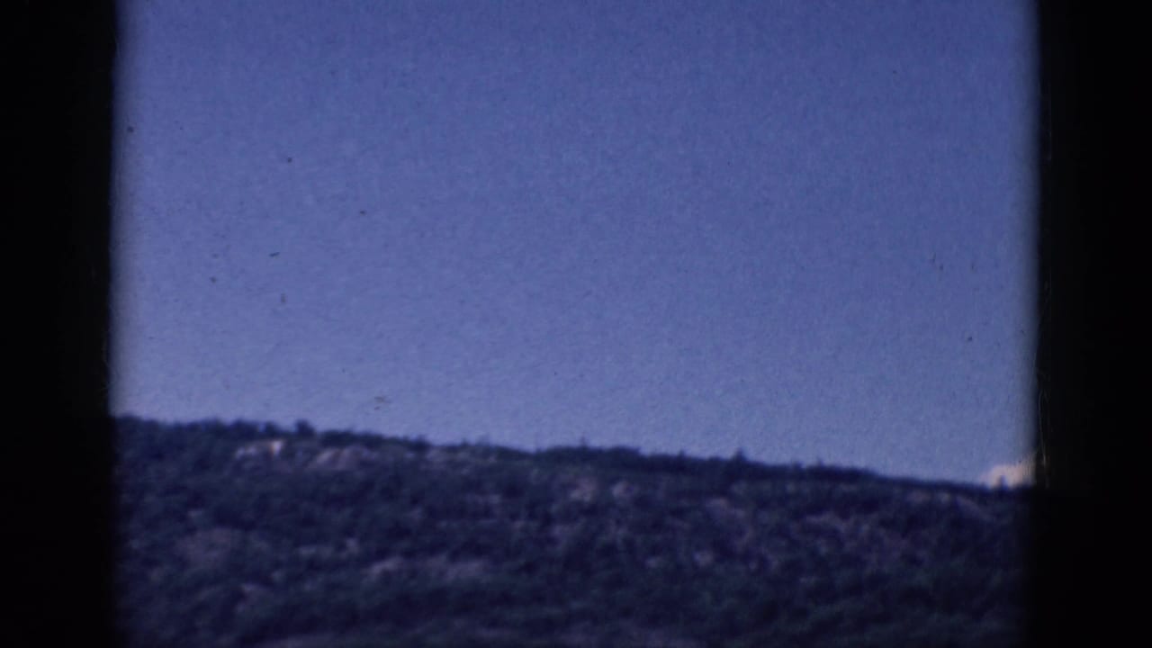 Blue sky and distant tree-covered ridge with dark vertical film borders.