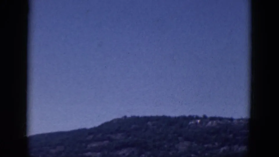 1968 8mm frame showing a distant hillside and open sky with visible grain and dark gate borders.